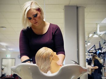 Frisørelev som vaskar hår på dukke Frisørelev som vaskar hår på dukke