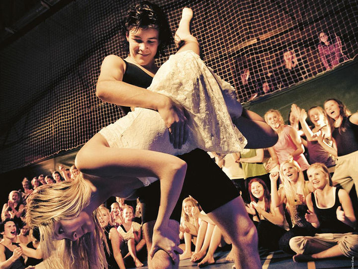 Foto som syner ei jente og ein gut som dansar. Guten er kledd i svart og held jenta, som er kledd i kvitt, opp-ned. Bak dei ser me ungdomar som er publikum.