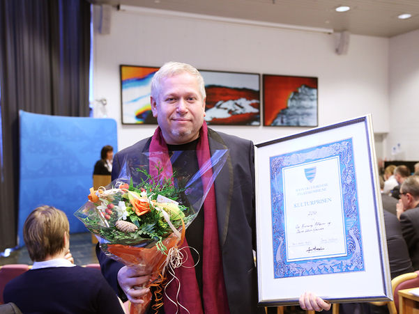 Foto av Ove Henning Solheim, som tok imot fylkeskulturprisen 2016 på vegne av seg sjølv og Dans Uten Grenser. Han held ein blomsterbukett i ei hand og diplomet for prisen i den andre. Bak han ser vi ein fullsett fylkestingssal.