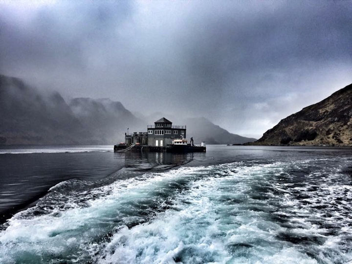 Illustrasjonsfoto: Marine Harvest Norway Foto av eit oppdrettsanlegg som ligg ute på sjøen. Vêret er grått, og skyene heng nedover fjellsidene i bakgrunnen.