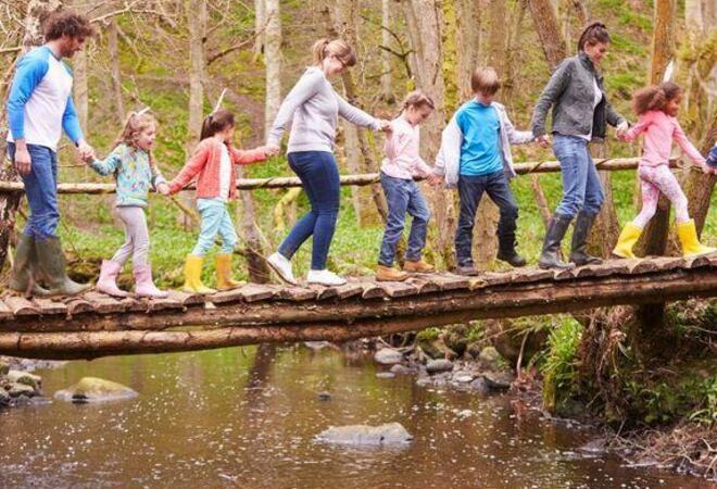 Barn og voksne som går over ei bro i skogen