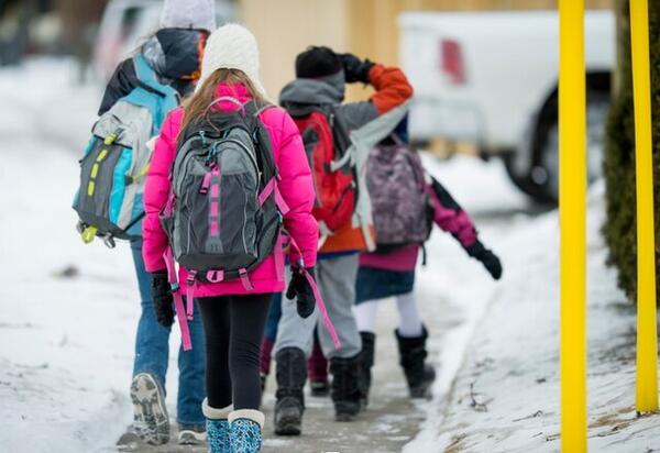 4 barn med skolesekk som går på fortau om vinteren