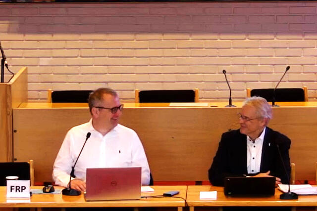 Ordfører og rådmann smiler til hverandre i kommunestyresalen.