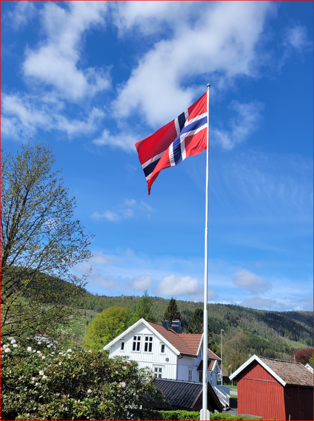 Norsk flagg , blå himmel, lensmannsgården i bakgrunnen