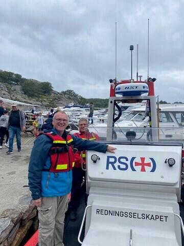 To menn i redningsvest står ved en båt merket med RS. De smiler.