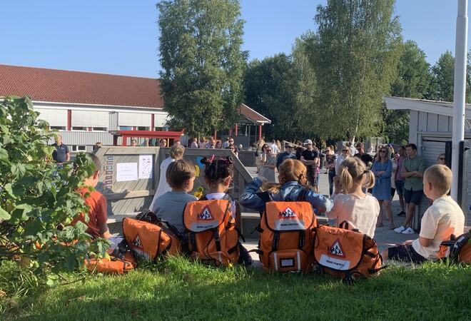 1. klasse elever med oransje skolesekk sitter på gressplenen.