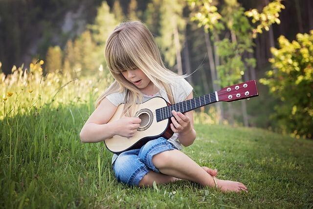 Ei lita jente som sitter i gresset og spiller gitar