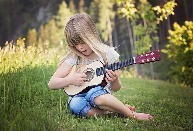 Ei lita jente som sitter i gresset og spiller gitar