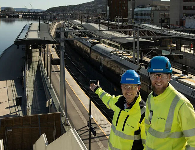 Geir Boman Rinde (til venstre) og Morten E. Paulsen er begge byggeledere for elektro på stasjonen. De viser fornøyde fram de første solcellepanelene som ble montert på plattformtaket ved elva. Foto: Anne Mette Storvik, Bane NOR