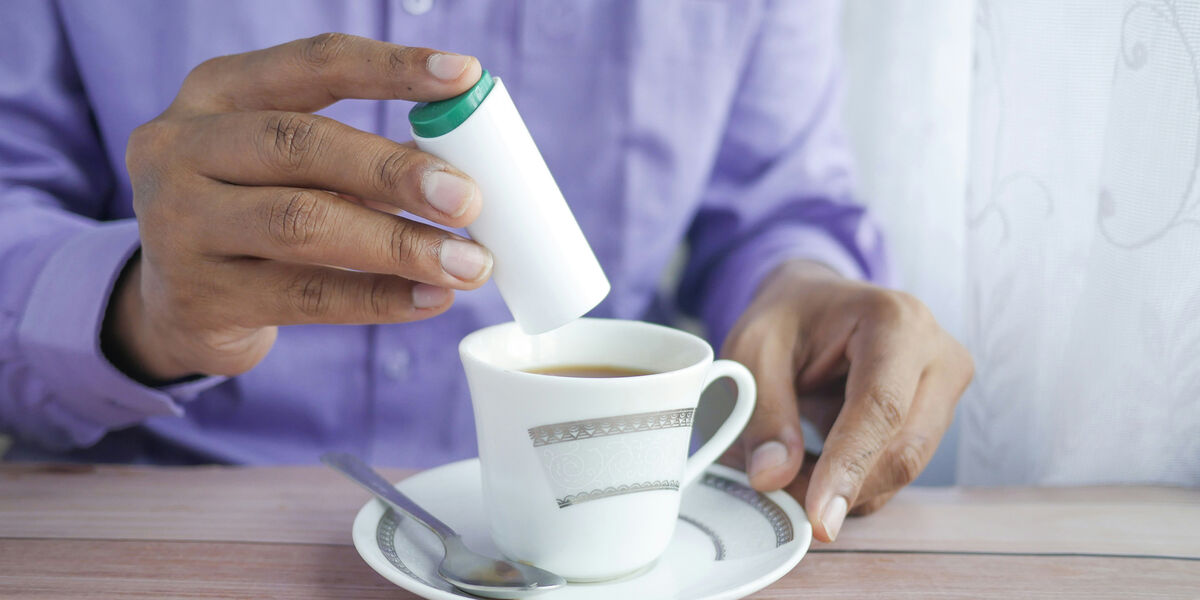 Photo of a cup of coffee with somebody pouring in some sweeteners