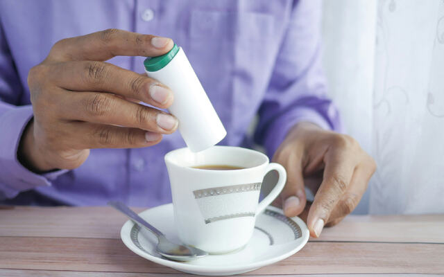 Photo of a cup of coffee with somebody pouring in some sweeteners