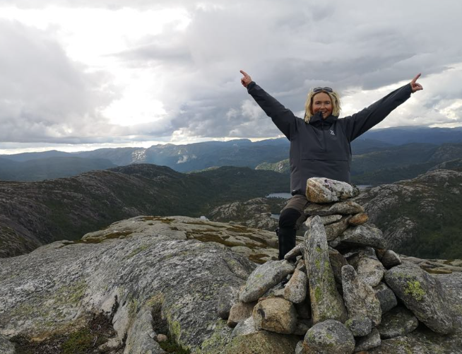 Ordfører Gro Helleland på toppen av ett fjell, med armene i været
