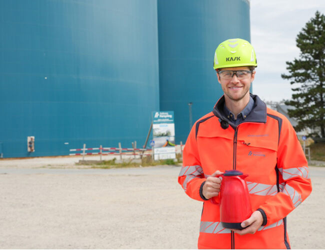 Akkumulatortanker kan sammenlignes med en termokanne, som prosjektlederen fra Aalborg Forsyning, Johan Kjep Nørgaard, holder i hånden. Tankene er bare i kjempeformat. I tankene lagres varmen når den er billigst å produsere, og brukes når behovet er størst. Foto: Aalborg Forsyning.